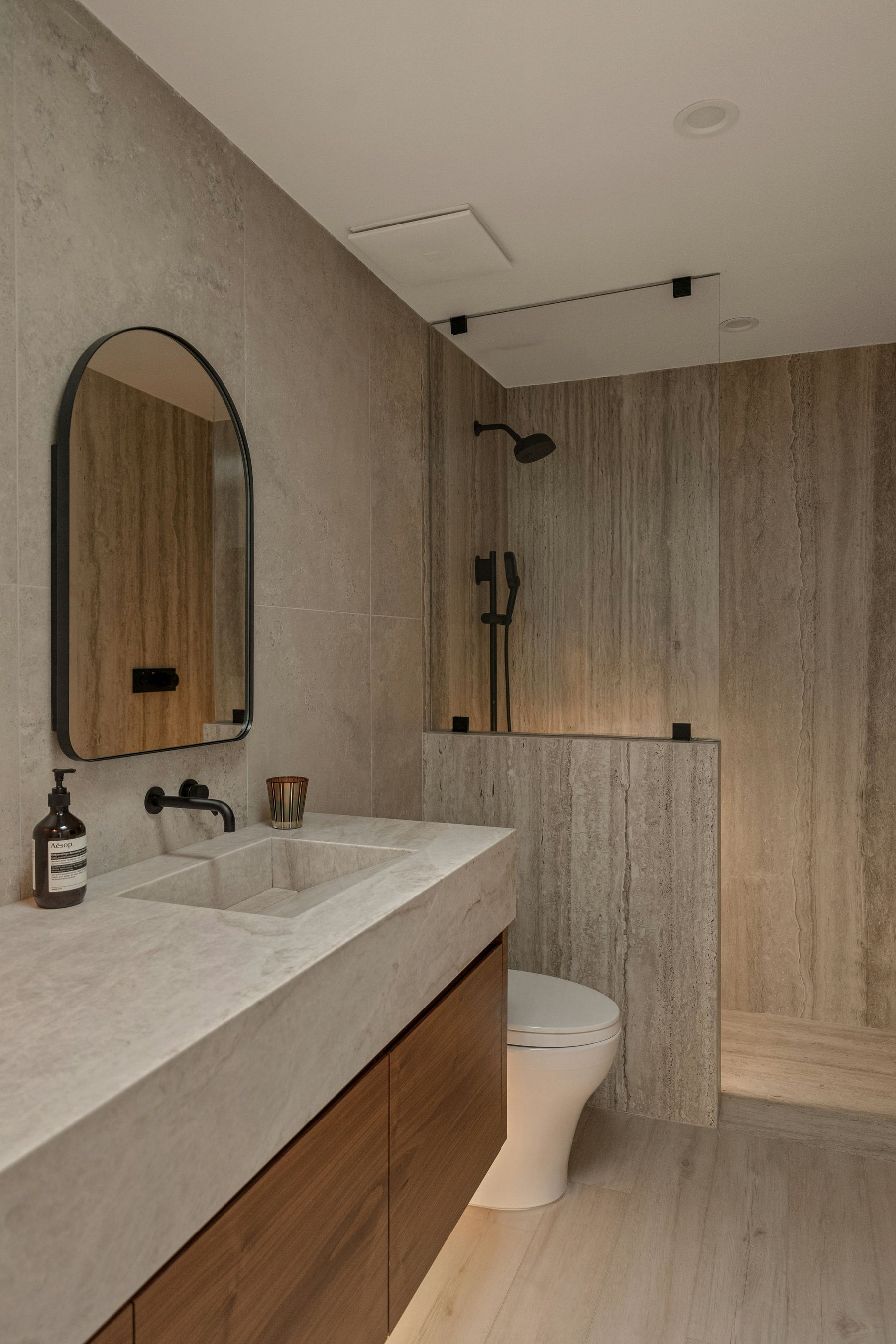 Modernes Badezimmer mit warmem Naturstein, Holz und indirekter Beleuchtung